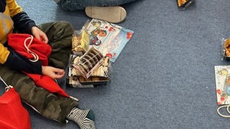 Children sitting in a circle, unpacking red gift bags containing books and cookies.